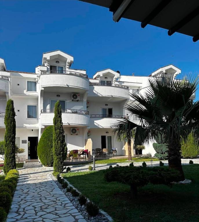 White resort buildings with balconies, palm trees and a stone path in the garden