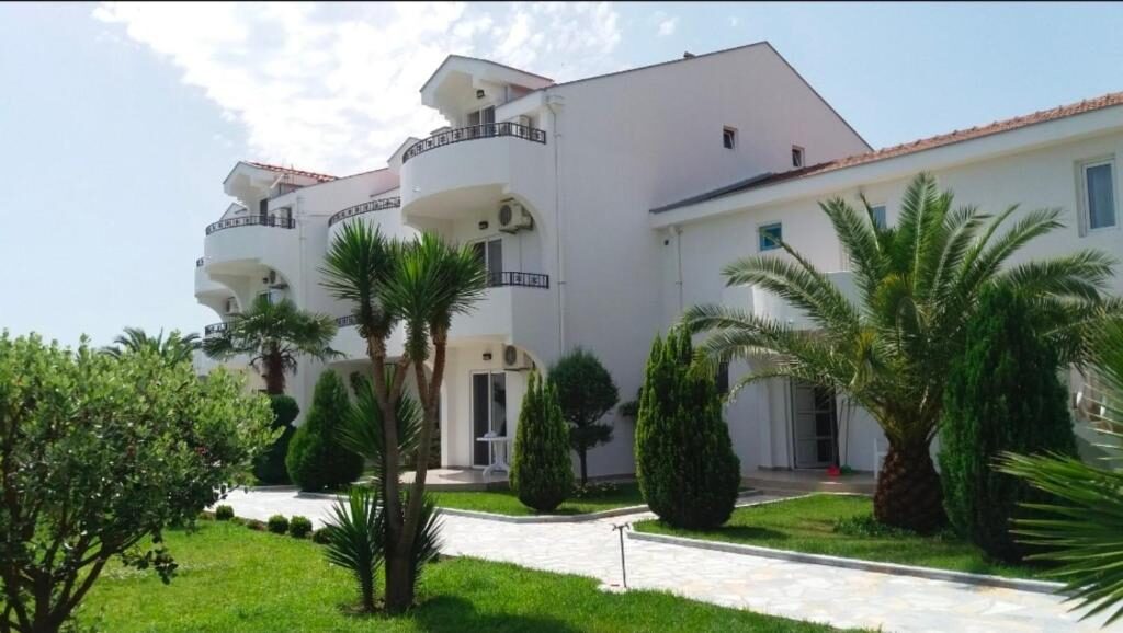 Garden with palm trees and stone paths in front of the white resort buildings in Ulcinj